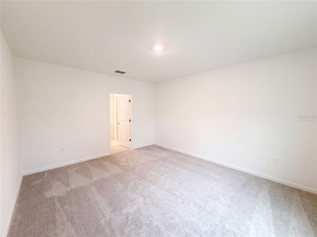 An empty bedroom with white walls, light gray carpeting, and a doorway leading to a bathroom — 5420 MEADOW WALK DRIVE, DAVENPORT, FL