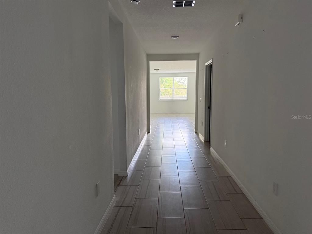 A long hallway with light-colored tile flooring leads toward a room with a window — 3098 LAUREL OAK LANE, WINTER HAVEN, FL