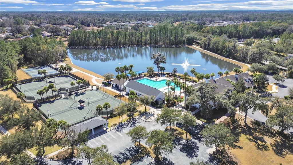 An aerial view shows a community clubhouse with a swimming pool, tennis courts, and lake — 4748 HICKORY OAK DRIVE, BROOKSVILLE, FL