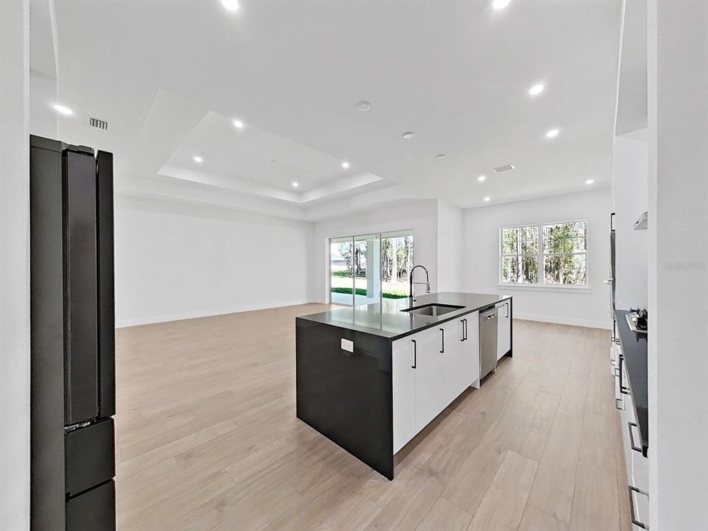 A modern kitchen features a black and white island, light wood flooring, and recessed lighting — 4748 HICKORY OAK DRIVE, BROOKSVILLE, FL