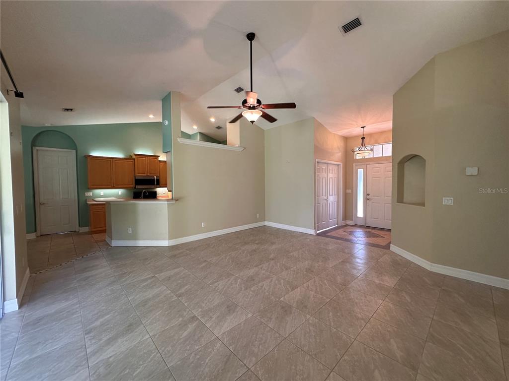 An open-concept living room features light-colored tile flooring, vaulted ceilings, and an adjacent kitchen area — 30 WILD FERN LANE, ORMOND BEACH, FL