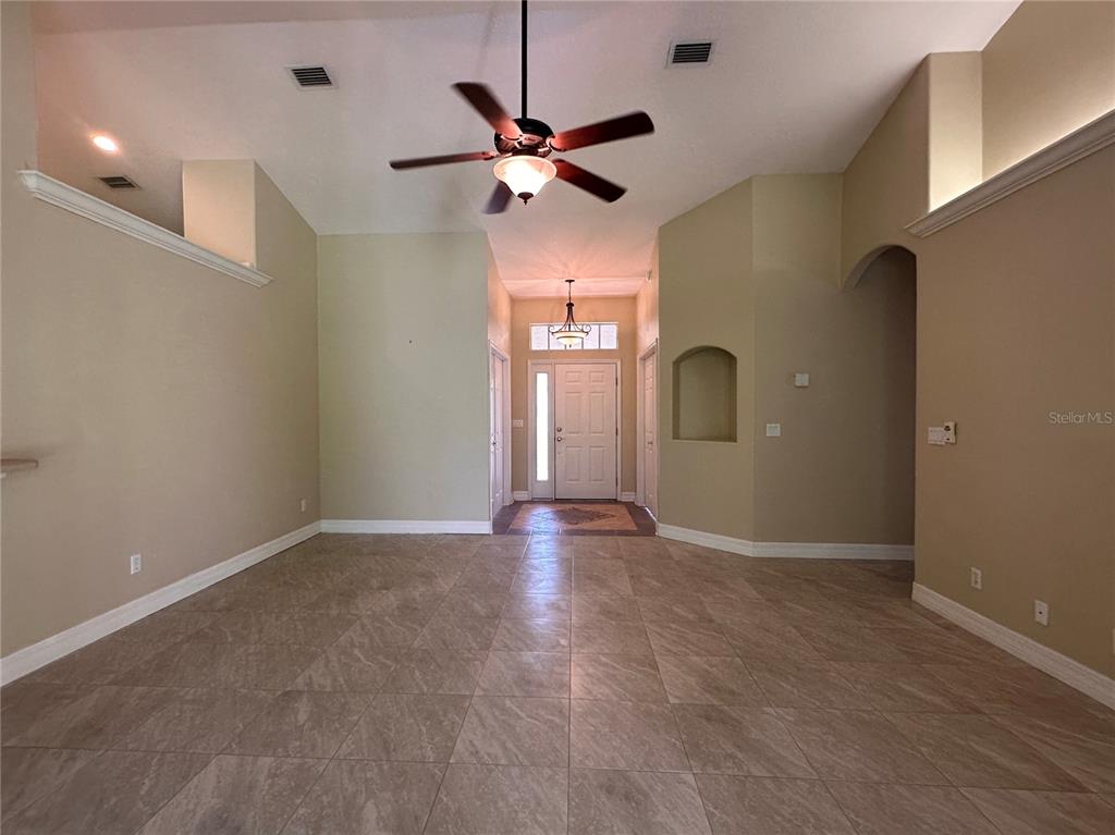 An empty room with beige walls, tile flooring, a ceiling fan, and a front entryway — 30 WILD FERN LANE, ORMOND BEACH, FL