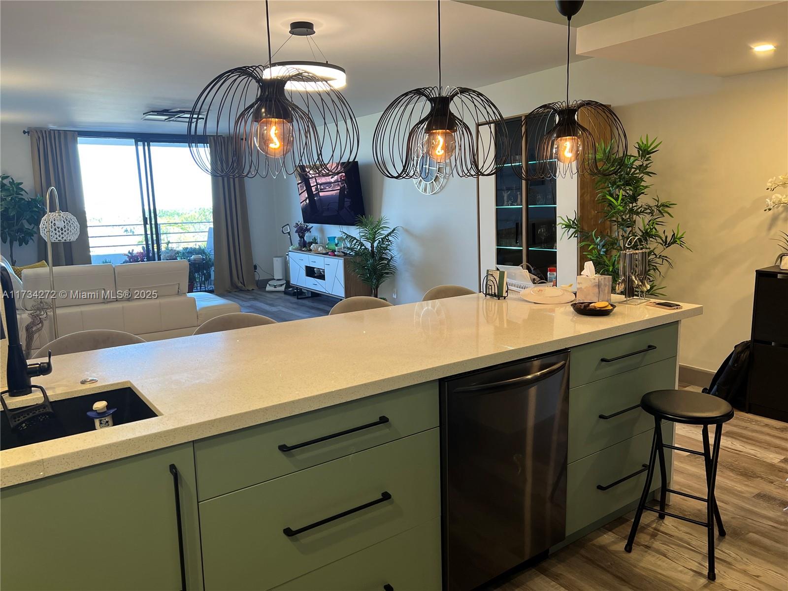 A kitchen island with sage green cabinets and a white countertop sits before a living area — 600 Three Islands Blvd # 504, Hallandale Beach FL 33009, HALLANDALE BEACH, FL