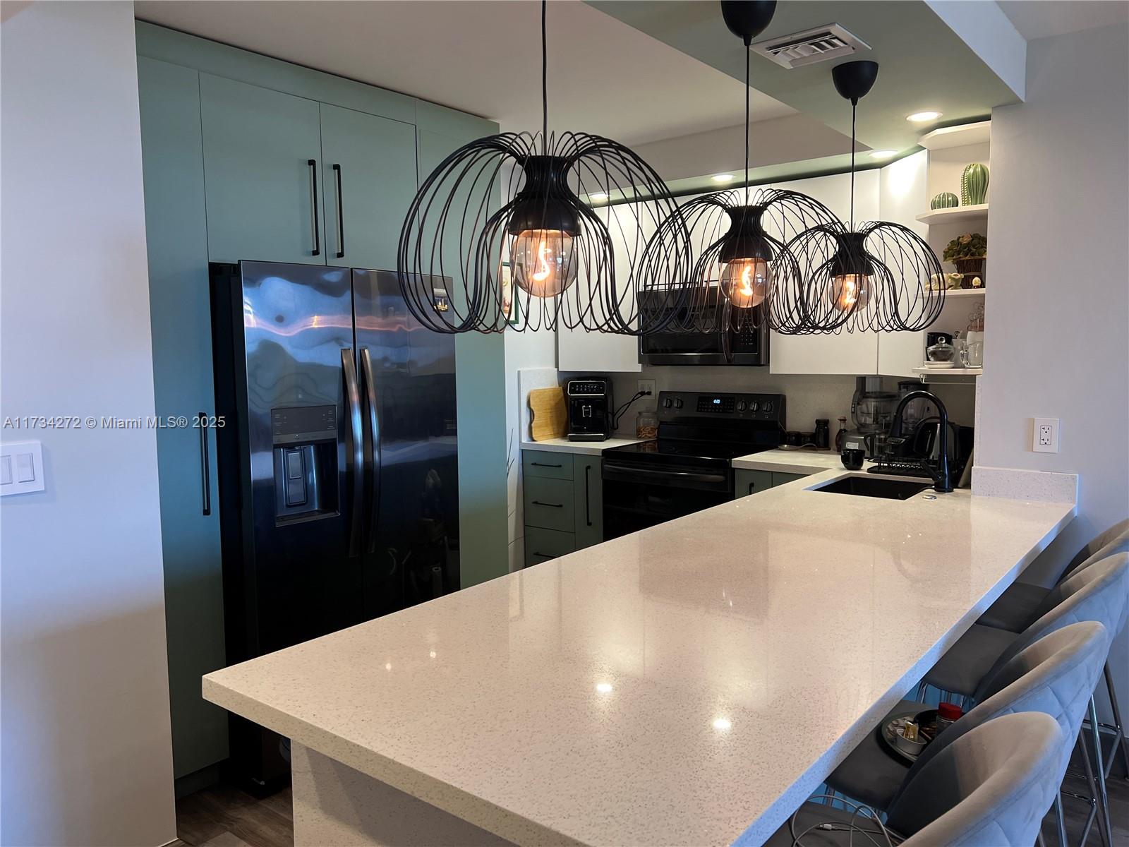 A kitchen features a white quartz island, teal cabinetry, black appliances, and three wire pendant lights — 600 Three Islands Blvd # 504, Hallandale Beach FL 33009, HALLANDALE BEACH, FL