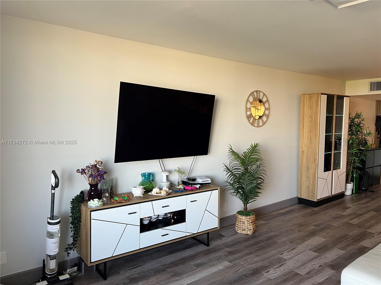 A living room features a wall-mounted television, a white and wood media console, and flooring — 600 Three Islands Blvd # 504, Hallandale Beach FL 33009, HALLANDALE BEACH, FL