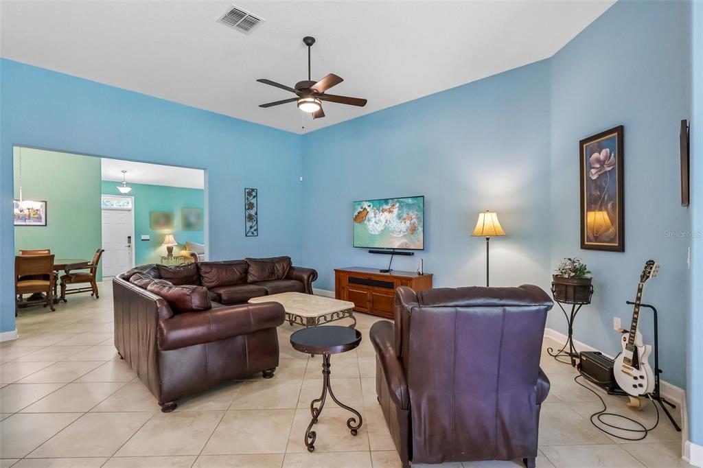 A living room features light blue walls, tile flooring, a brown leather sofa, and armchair — 8976 DOVE VALLEY WAY, DAVENPORT, FL