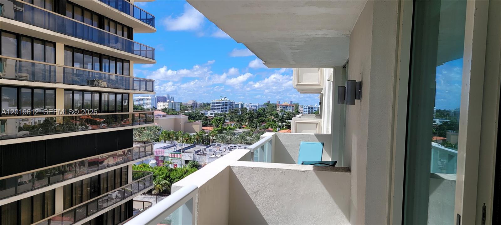 A balcony with a glass railing overlooks a neighboring building and a city skyline — 9499 Collins Ave # 705, Surfside FL 33154, SURFSIDE, FL