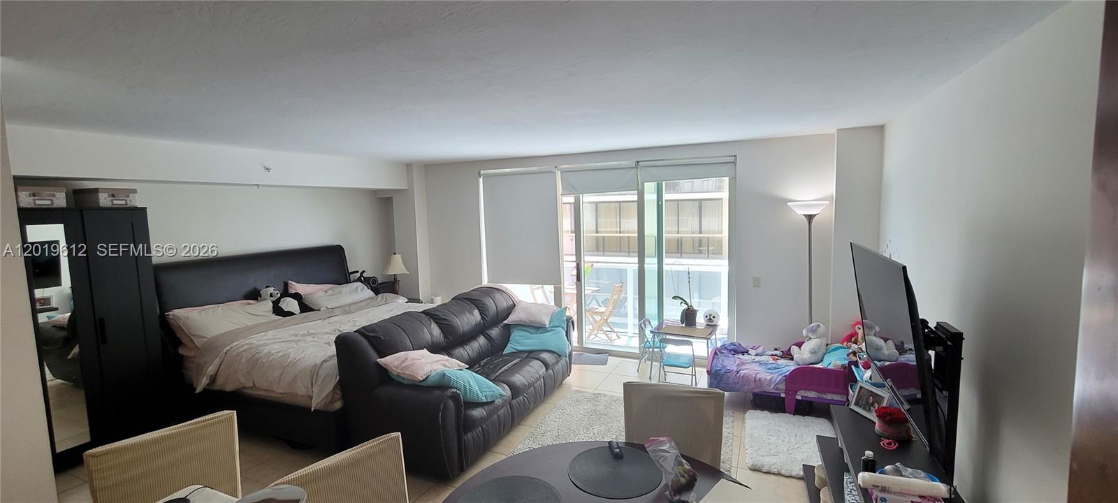 A studio apartment features a bed, a sofa, a dining table, and a balcony door — 9499 Collins Ave # 705, Surfside FL 33154, SURFSIDE, FL