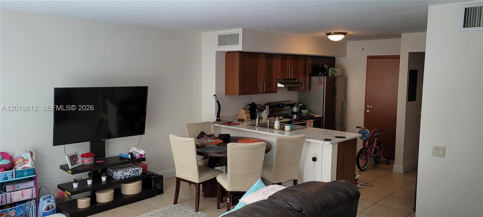 This open-concept living area features a dining table, kitchen with wood cabinets, and television — 9499 Collins Ave # 705, Surfside FL 33154, SURFSIDE, FL
