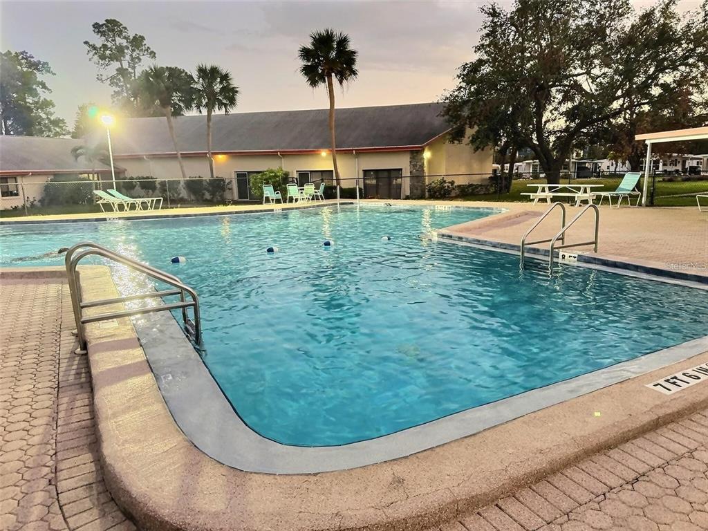 An outdoor swimming pool with metal ladders and surrounding patio furniture near a residential building — 667 SUGAR PALM STREET, LARGO, FL