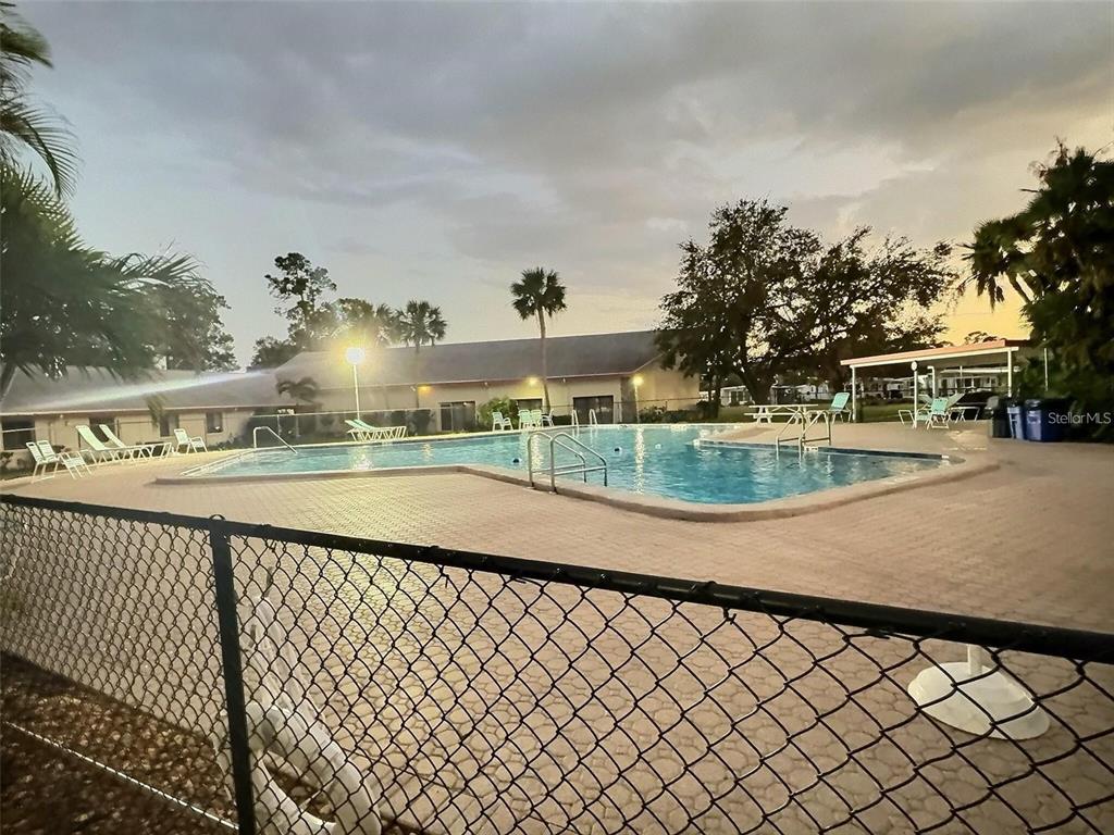 An outdoor swimming pool with a surrounding patio and chain-link fence at dusk — 667 SUGAR PALM STREET, LARGO, FL