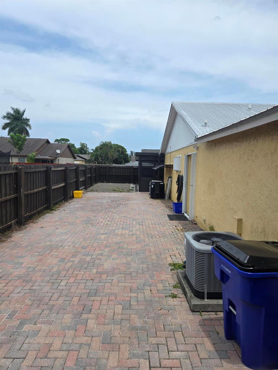 A paved side yard features a wooden fence, an HVAC unit, and a blue bin — 1402 Denlow Lane, Royal Palm Beach FL 33411, ROYAL PALM BEACH, FL