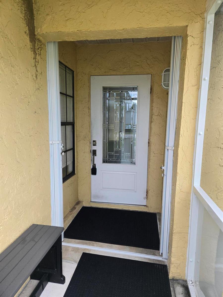 A white front door with a decorative glass insert sits within a yellow stucco entryway — 1402 Denlow Lane, Royal Palm Beach FL 33411, ROYAL PALM BEACH, FL
