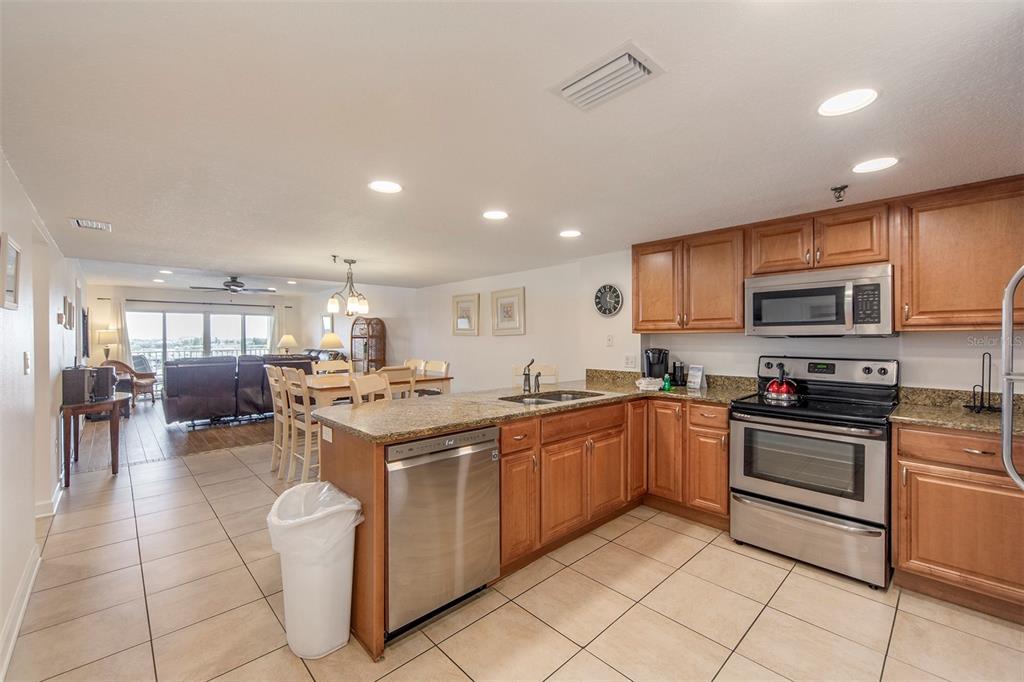 A kitchen with wood cabinets and stainless steel appliances opens into a dining and living area — 12901 GULF LANE UNIT 503, MADEIRA BEACH, FL