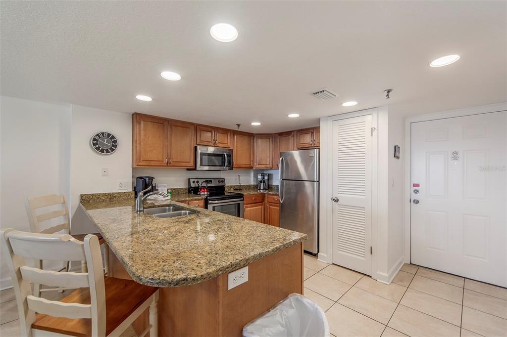 A kitchen features wood cabinets, granite countertops, stainless steel appliances, and a breakfast bar — 12901 GULF LANE UNIT 503, MADEIRA BEACH, FL