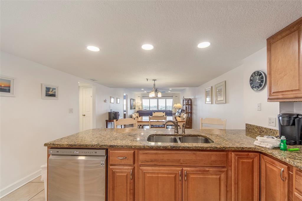 A kitchen with granite countertops and wood cabinets overlooks a dining area and living room — 12901 GULF LANE UNIT 503, MADEIRA BEACH, FL