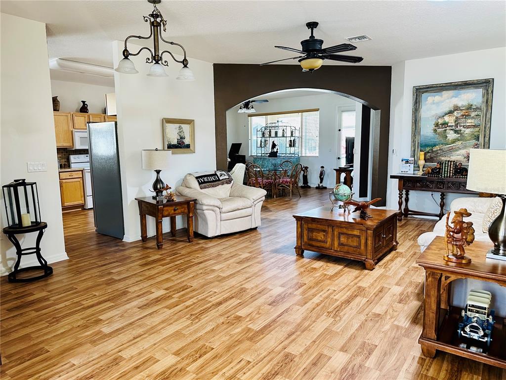 A living room with wood-look flooring, a ceiling fan, and an arched opening to a dining area — 9053 SW 103RD AVENUE, OCALA, FL