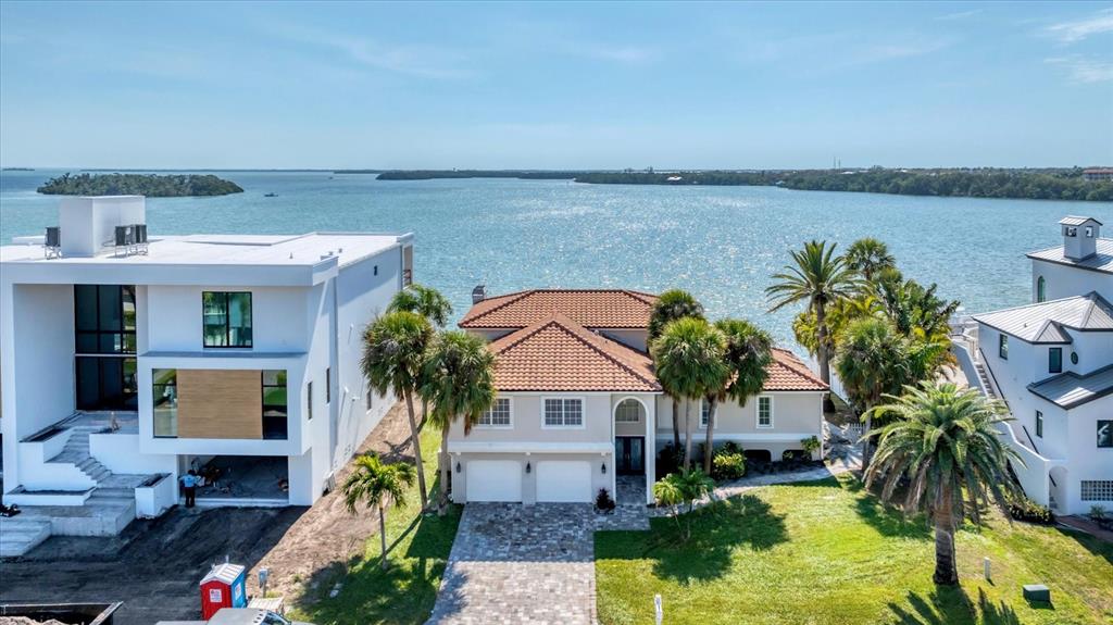An aerial view shows a two-story house with a tiled roof situated between two modern homes — 120 SANDS POINT DRIVE, TIERRA VERDE, FL