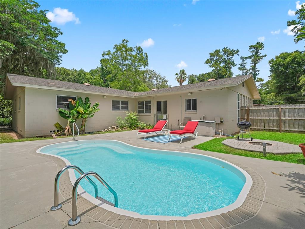 A backyard features a swimming pool, two red lounge chairs, and a charcoal grill — 1520 NE 12TH STREET, OCALA, FL