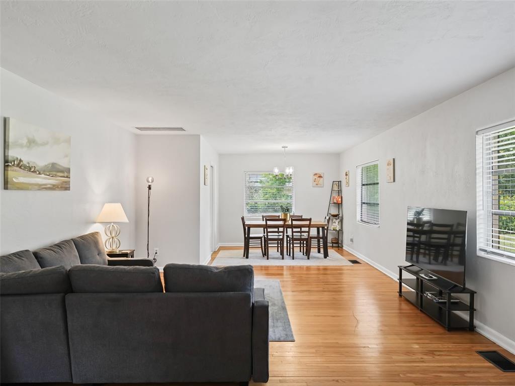 A living room and dining area with hardwood floors, a gray sofa, and a television — 1520 NE 12TH STREET, OCALA, FL