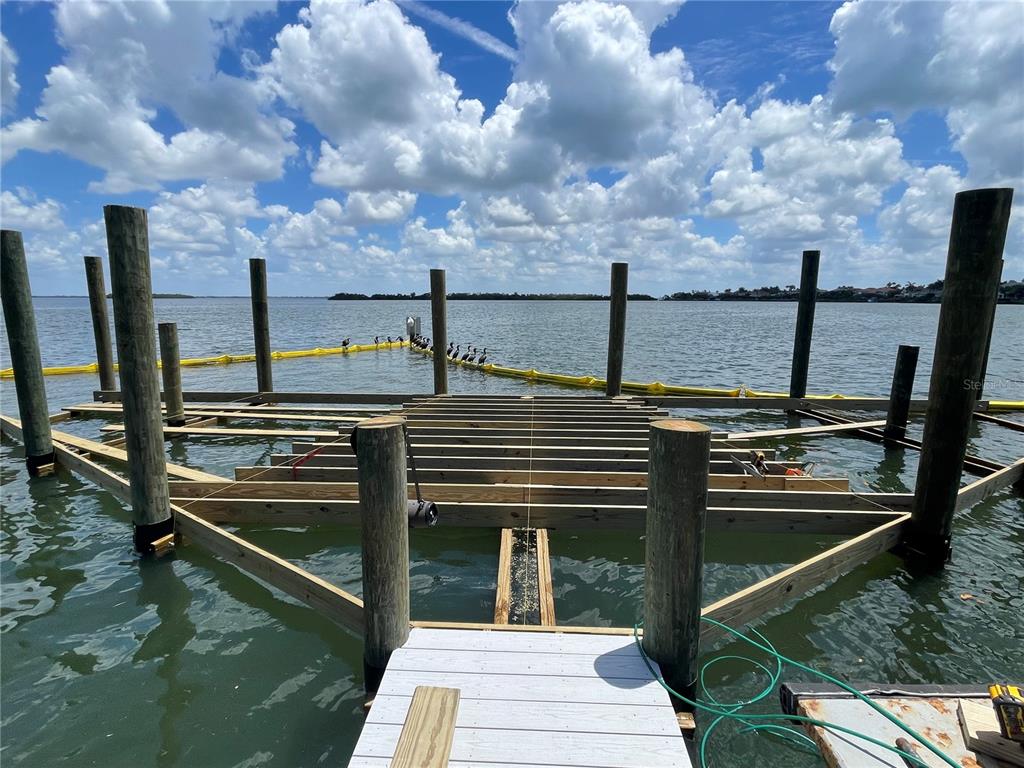 A wooden dock under construction extends over the water with pilings and framing visible — 3710 GULF OF MEXICO DRIVE UNIT G12, LONGBOAT KEY, FL