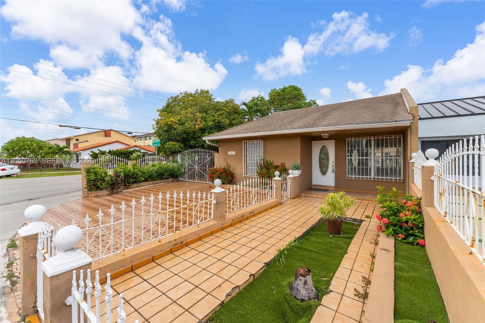 A single-story house features a tiled front yard, white metal fencing, and a paved walkway — 10873 NW 1st Ln # 10873, Miami FL 33172, MIAMI, FL