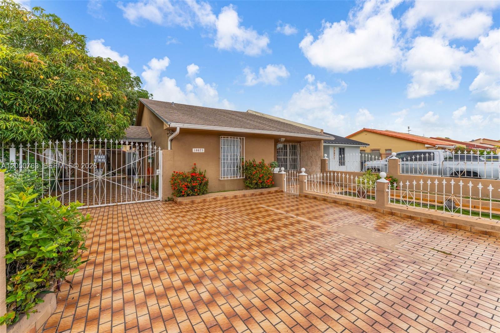 A single-story house with a paved driveway and white metal fencing under a blue sky — 10873 NW 1st Ln # 10873, Miami FL 33172, MIAMI, FL