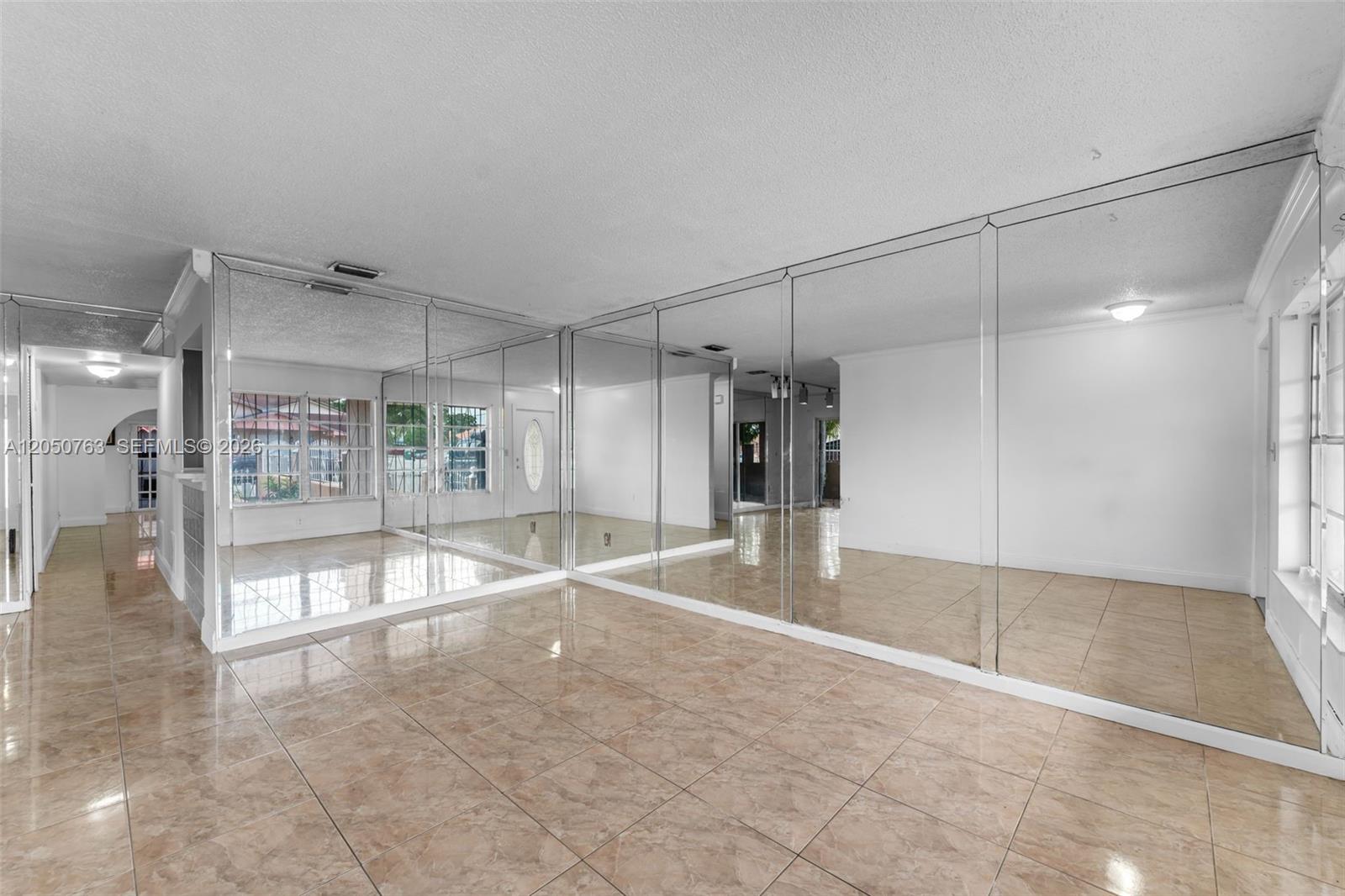 A room with beige tile flooring and large mirrored walls reflecting the interior space — 10873 NW 1st Ln # 10873, Miami FL 33172, MIAMI, FL