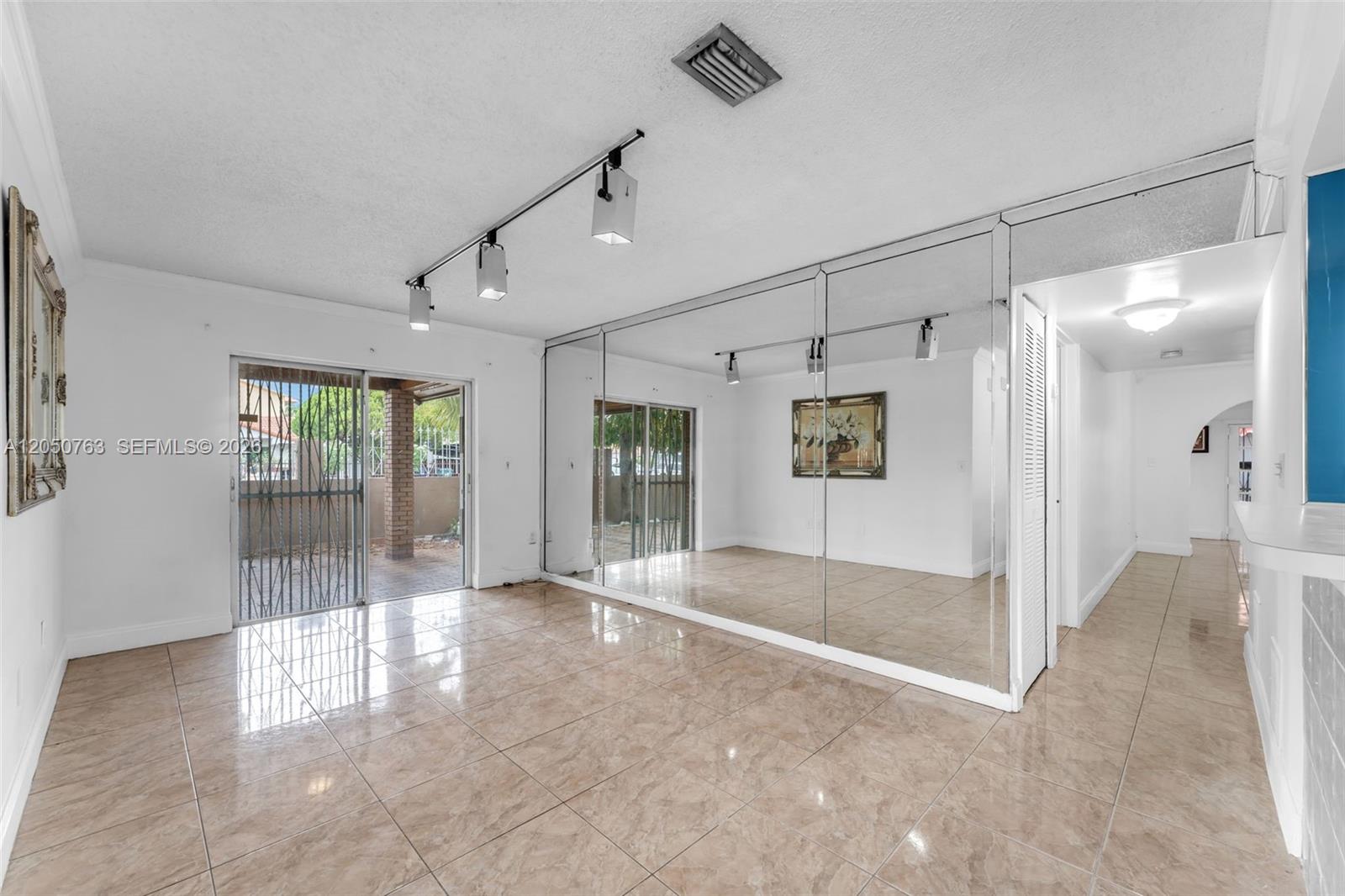 A room with beige tile flooring, a mirrored wall, and a sliding glass door — 10873 NW 1st Ln # 10873, Miami FL 33172, MIAMI, FL