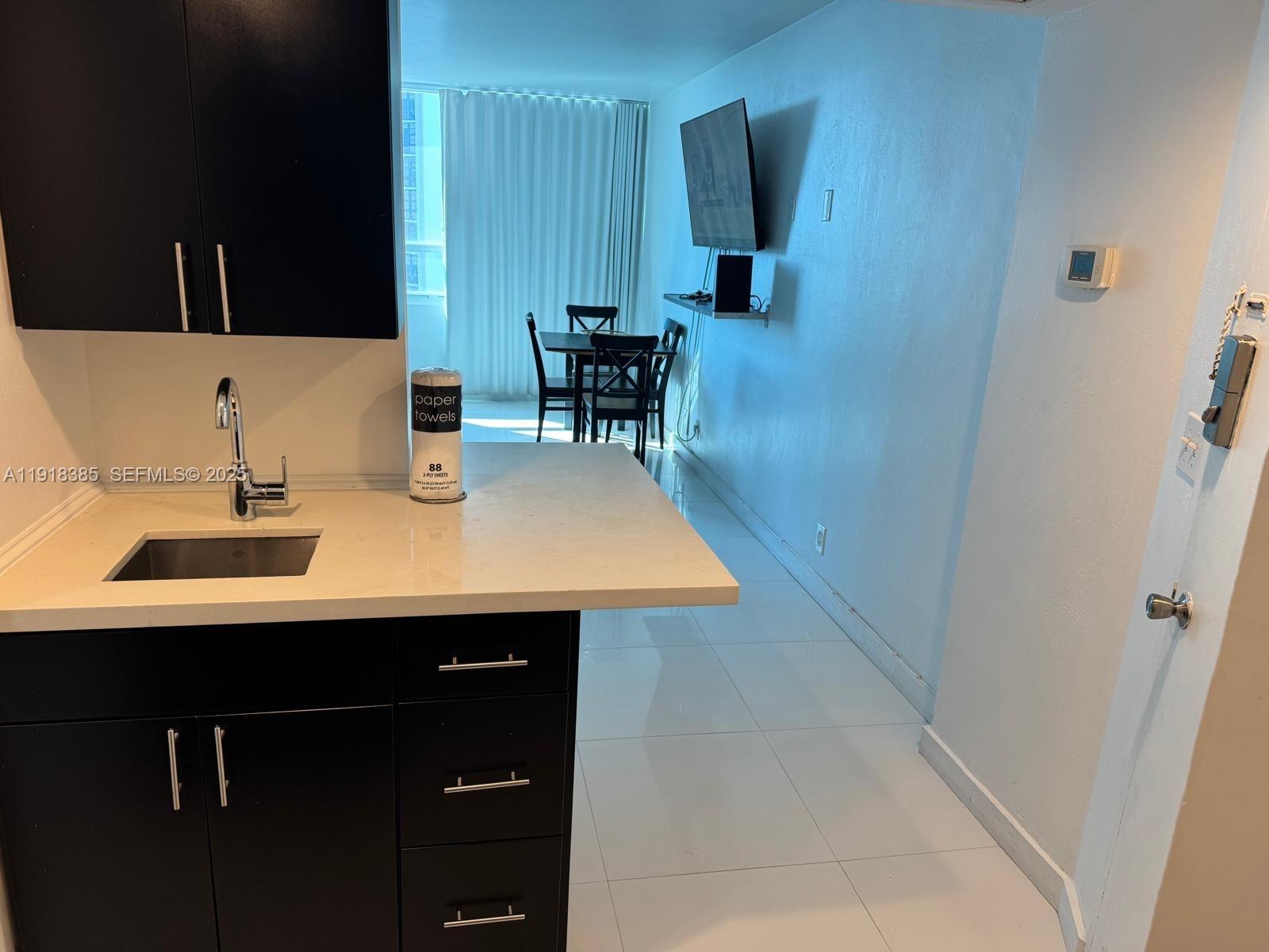 A kitchen with dark cabinets and white countertops overlooks a dining area and living space — 5445 Collins Ave # 915, Miami Beach FL 33140, MIAMI BEACH, FL