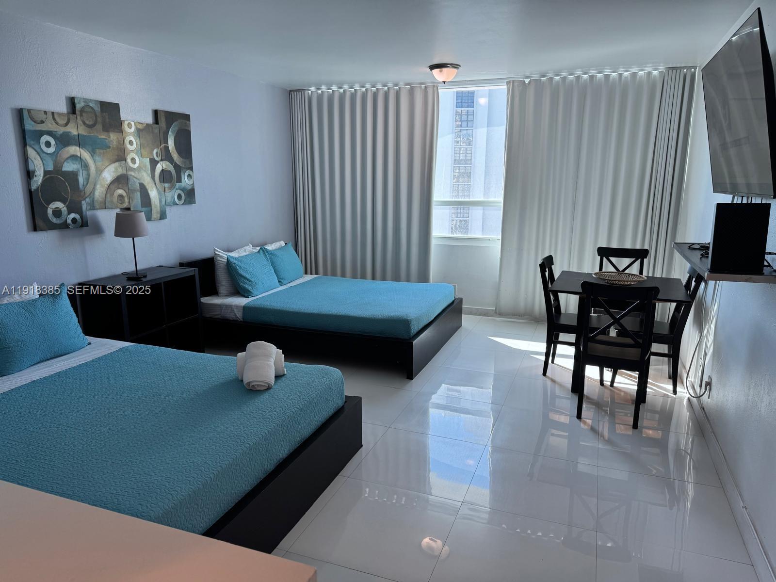 A hotel room features two beds with blue bedding, a dining set, and tiled floors — 5445 Collins Ave # 915, Miami Beach FL 33140, MIAMI BEACH, FL
