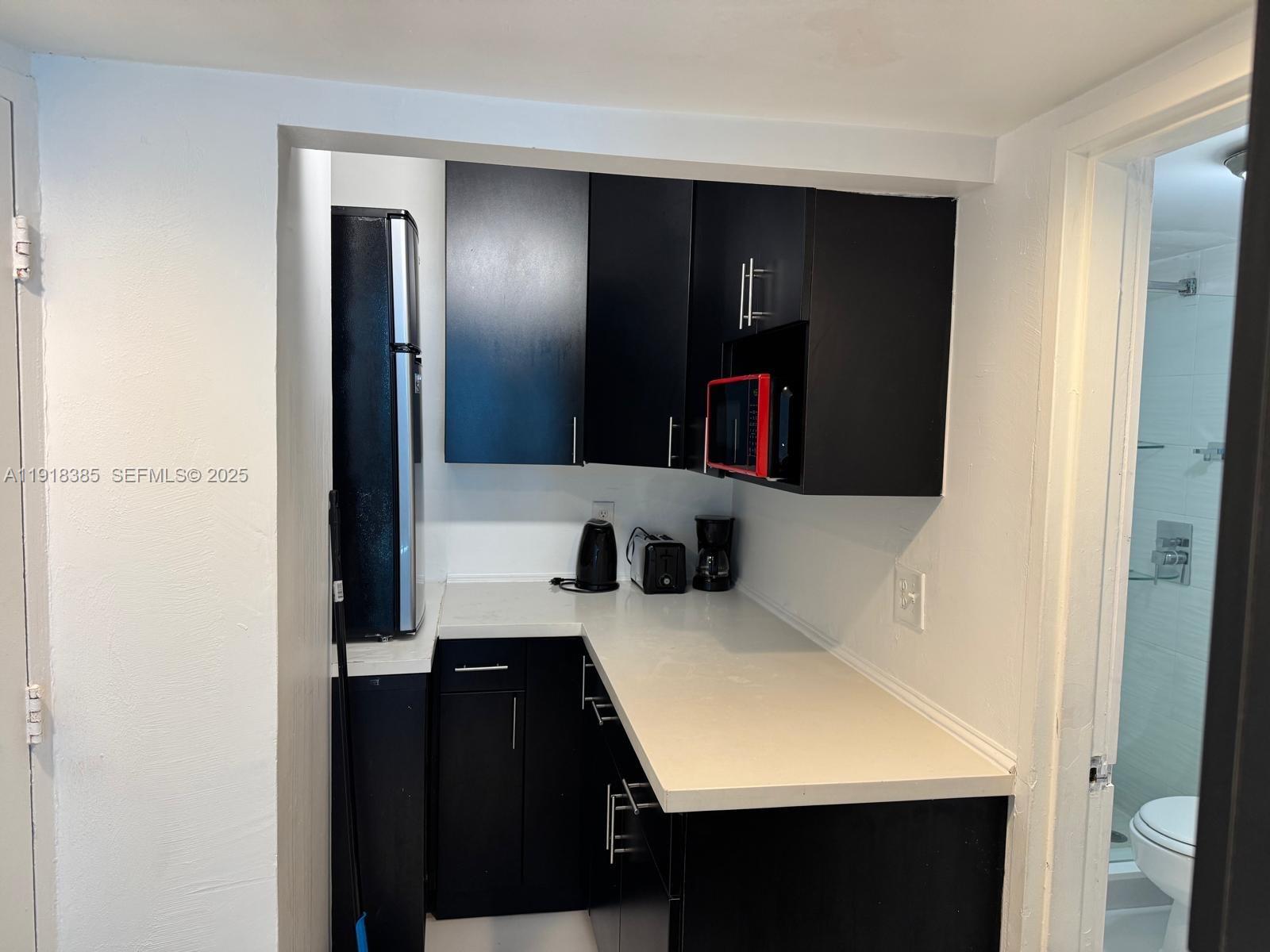 A small kitchen features black cabinets, white countertops, and a black refrigerator — 5445 Collins Ave # 915, Miami Beach FL 33140, MIAMI BEACH, FL
