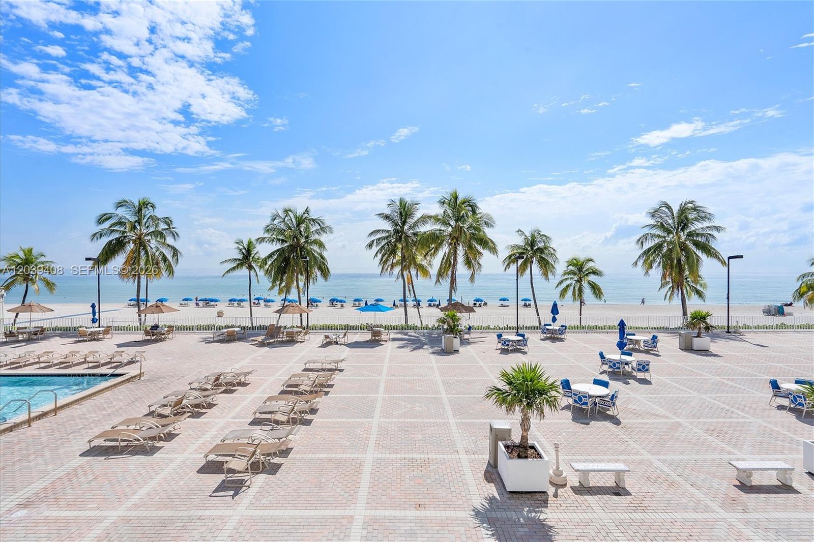 A paved pool deck features lounge chairs, tables, and palm trees overlooking a sandy beach — 2301 S Ocean Dr # 1406, Hollywood FL 33019, HOLLYWOOD, FL