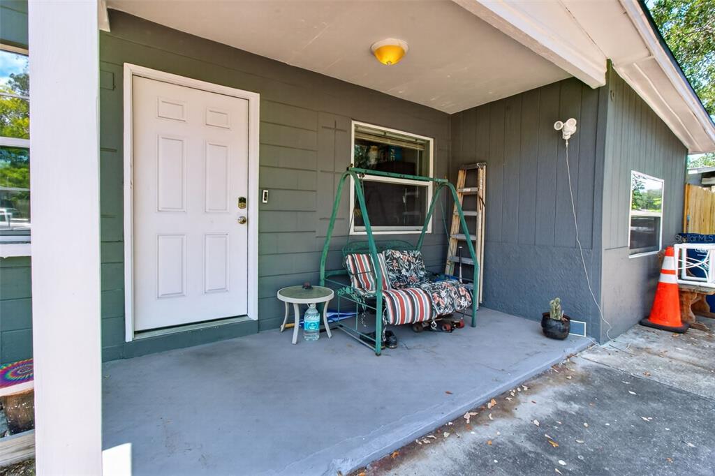A covered front porch features a white door, a metal swing, and a small table — 7772 90TH WAY, SEMINOLE, FL