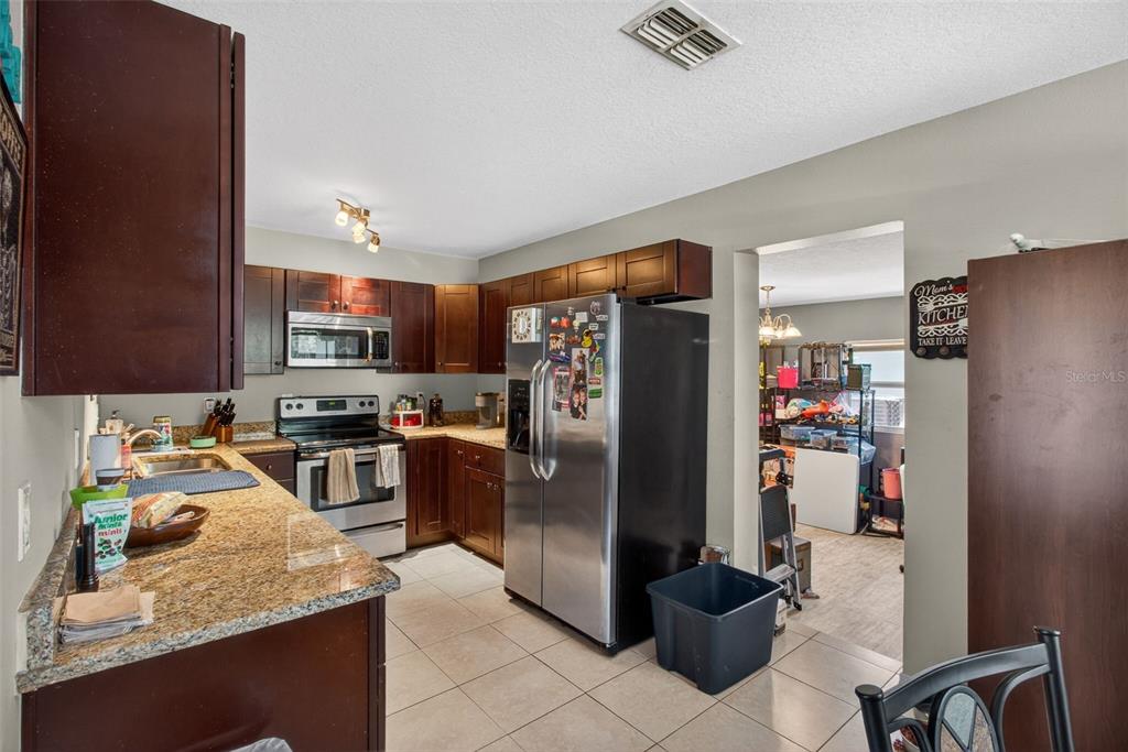 A kitchen with dark wood cabinets, granite countertops, stainless steel appliances, and tile flooring — 7772 90TH WAY, SEMINOLE, FL