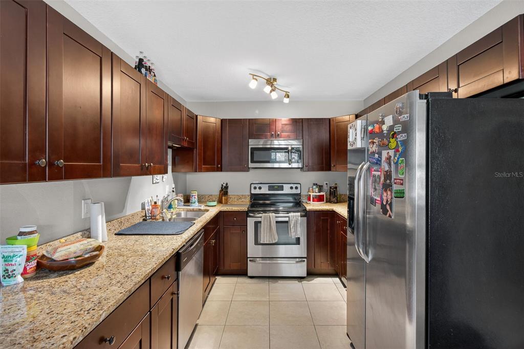 A kitchen features dark wood cabinets, granite countertops, stainless steel appliances, and tile flooring — 7772 90TH WAY, SEMINOLE, FL