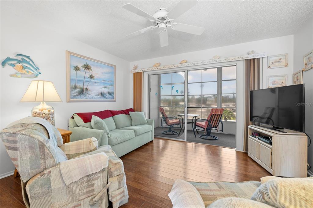 A living room features a light green sofa, patterned armchairs, wood flooring, and a sliding door — 5157 SILENT LOOP UNIT 208, NEW PORT RICHEY, FL