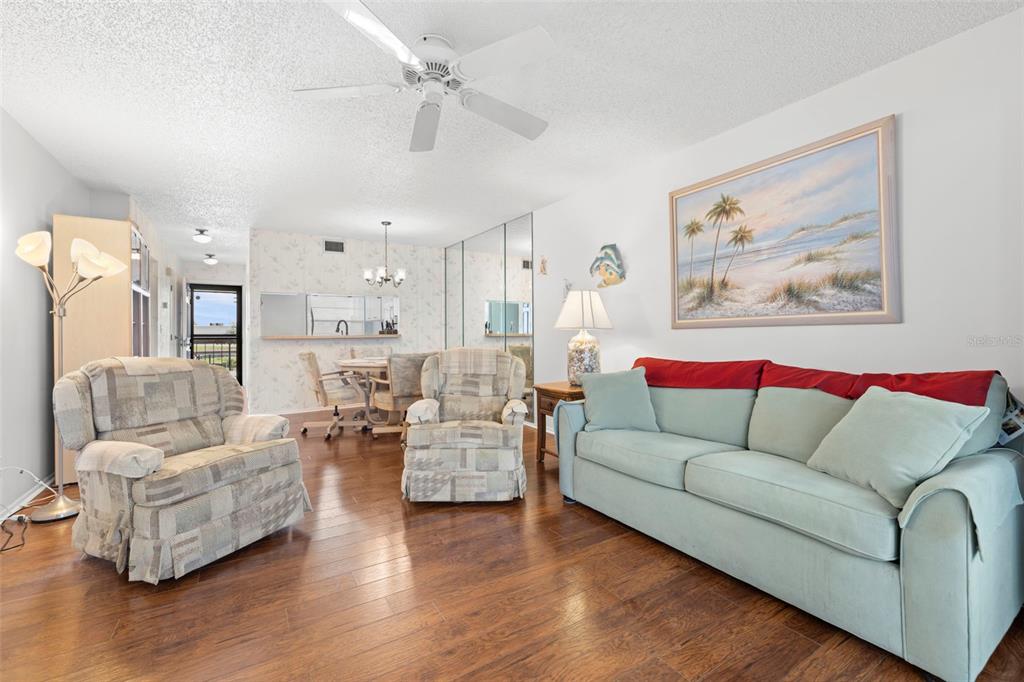 A living room features hardwood floors, a light blue sofa, two patterned armchairs, and a dining area — 5157 SILENT LOOP UNIT 208, NEW PORT RICHEY, FL
