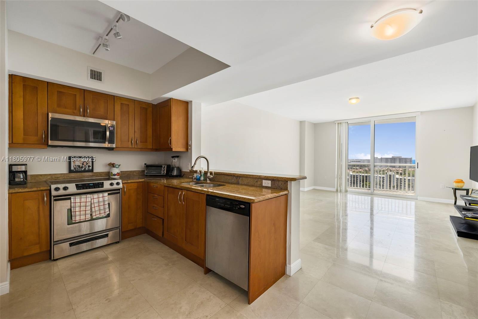 A kitchen with wood cabinets and stainless steel appliances opens to a bright living area — 1755 E Hallandale Beach Blvd # 1604E, Hallandale Beach FL 33009, HALLANDALE BEACH, FL