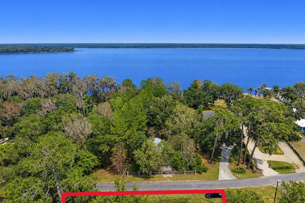 An aerial view shows a wooded lot bordering a large lake with a paved road — 21103 NE 117TH AVENUE, WALDO, FL