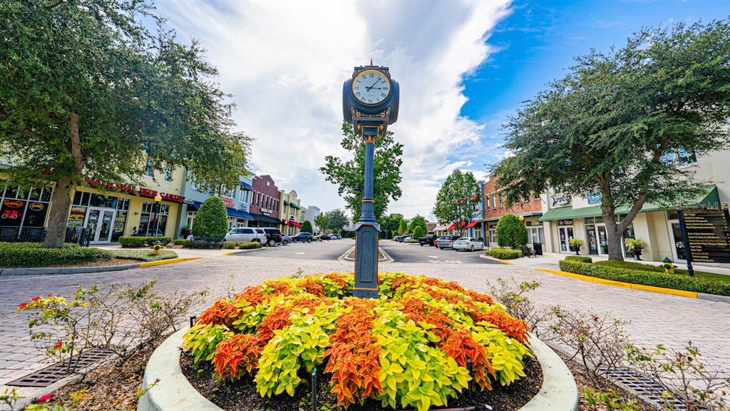 A street-level view of a brick-paved town center featuring a central clock tower and landscaping — 16540 POINTE VILLAGE DRIVE UNIT 206, LUTZ, FL