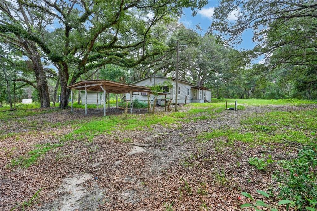 A single-story house with a carport sits on a large, wooded lot with scattered leaves — 130 WINDY HILLS ROAD, HAWTHORNE, FL