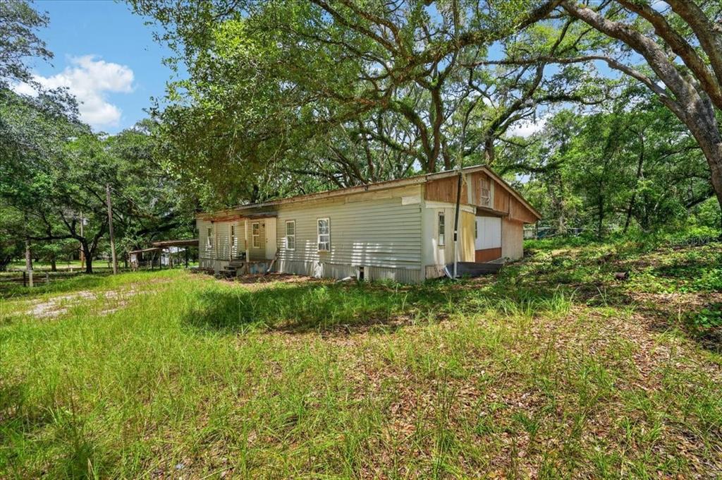 A weathered, single-story mobile home sits on a grassy lot surrounded by large oak trees — 130 WINDY HILLS ROAD, HAWTHORNE, FL