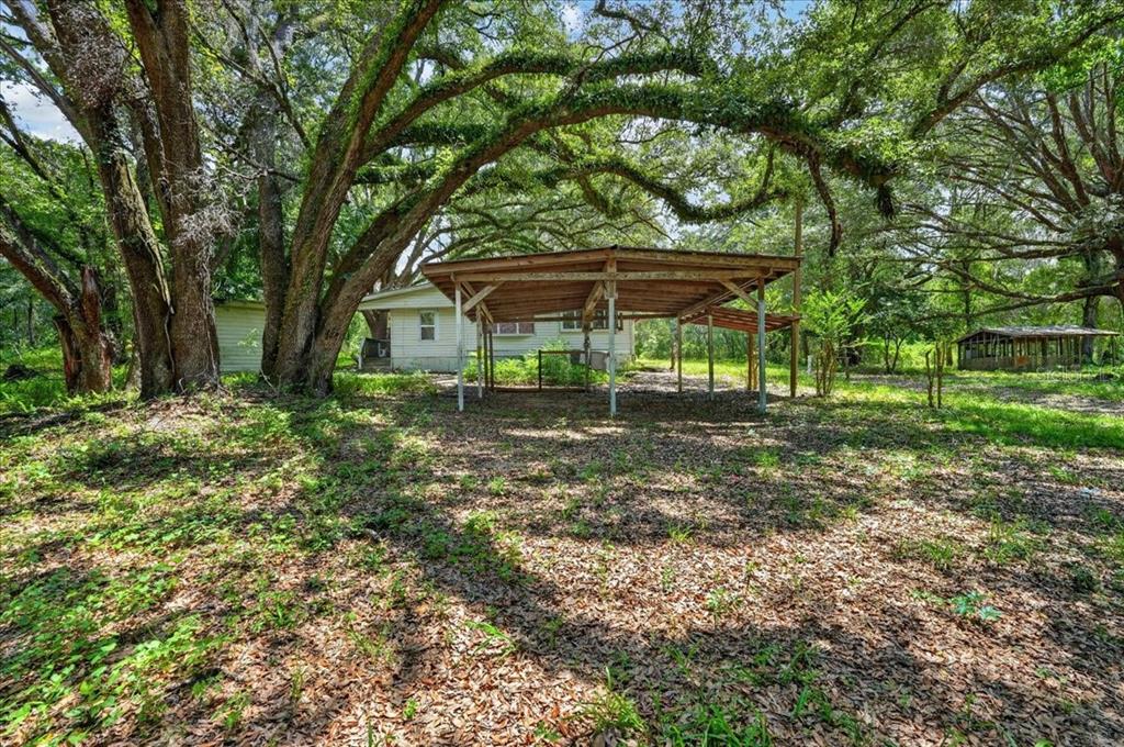 A wooden carport stands in front of a house surrounded by large, mature oak trees — 130 WINDY HILLS ROAD, HAWTHORNE, FL