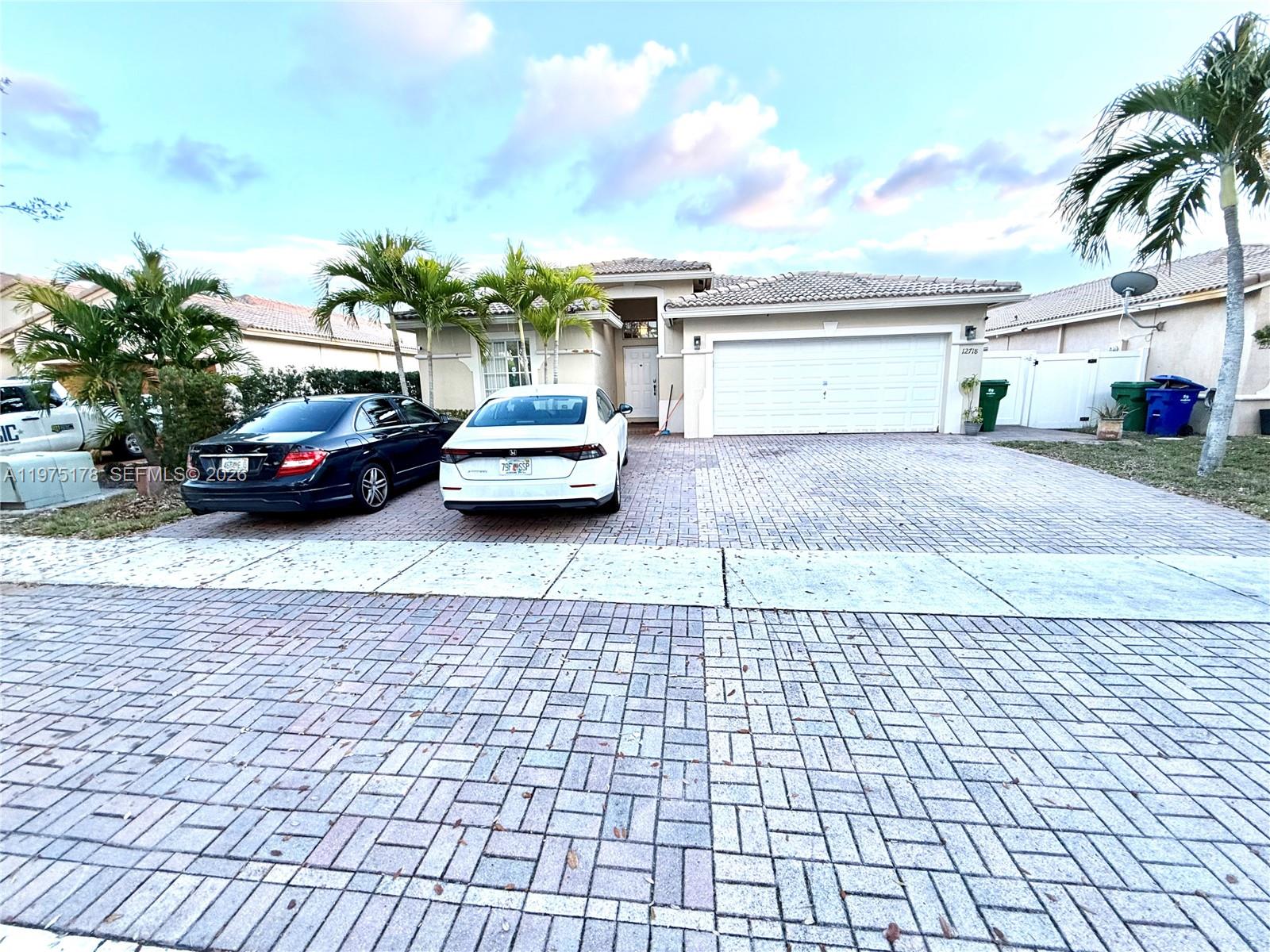 A one-story house with a paved driveway, two parked cars, and palm trees — 12718 SW 47th St, Miramar FL 33027, MIRAMAR, FL