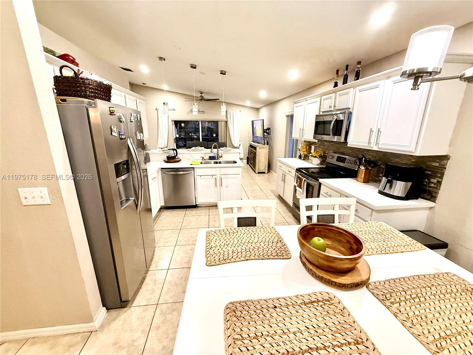 A kitchen with white cabinets, stainless steel appliances, and a dining table in the foreground — 12718 SW 47th St, Miramar FL 33027, MIRAMAR, FL