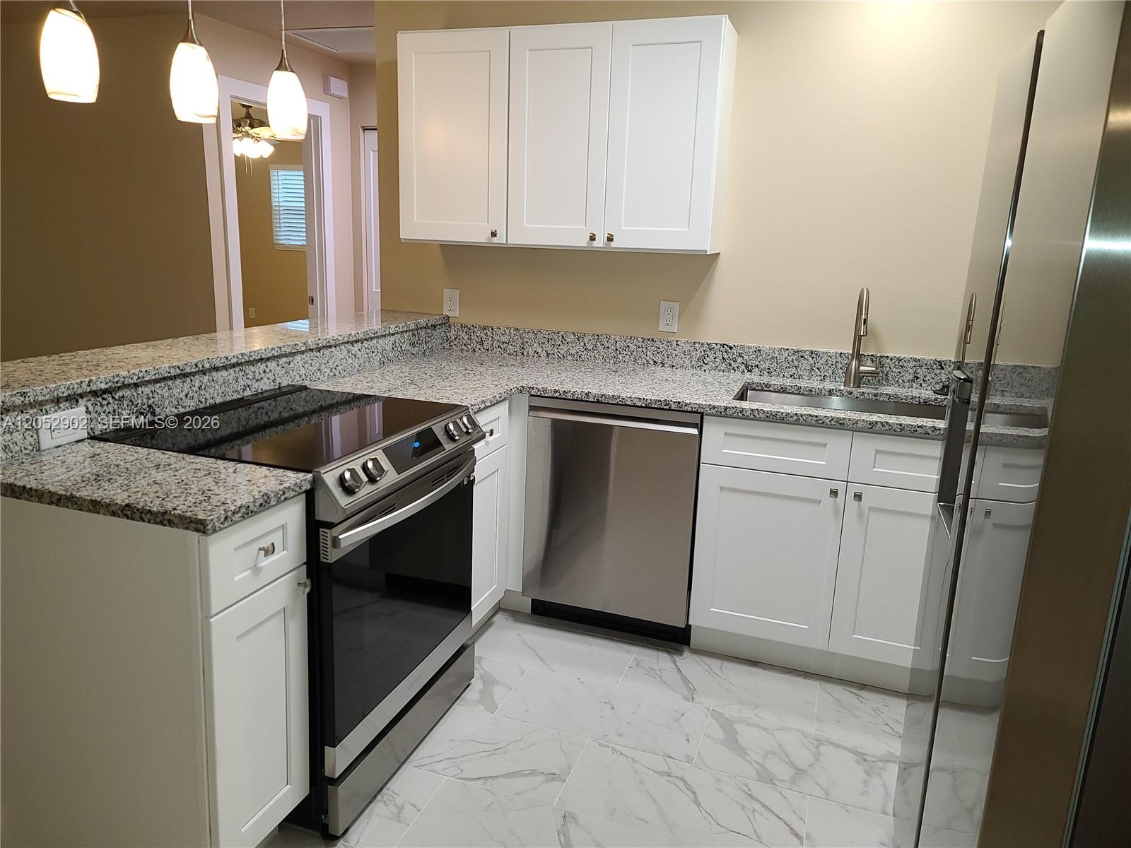 A kitchen features white cabinets, granite countertops, stainless steel appliances, and marble-look tile flooring — 4491 SE Roaring Brook Way # 4491, Stuart FL 34997, STUART, FL