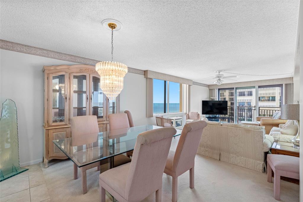 A dining area with a glass table and chandelier opens into a living room with ocean views — 1430 GULF BOULEVARD UNIT 501, CLEARWATER BEACH, FL