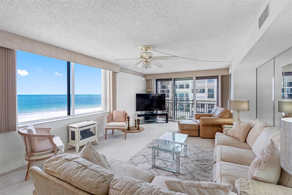 A living room features a large window with an ocean view, beige furniture, and carpet — 1430 GULF BOULEVARD UNIT 501, CLEARWATER BEACH, FL