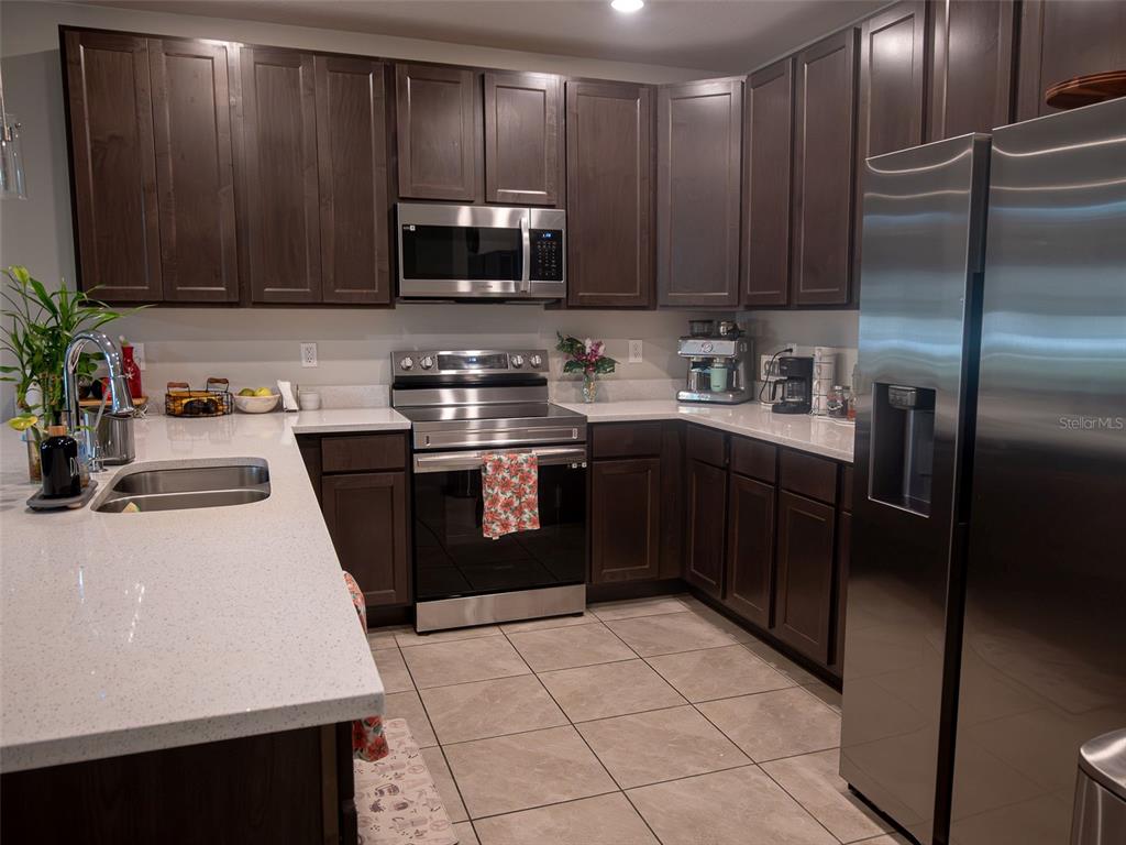 A kitchen features dark wood cabinets, stainless steel appliances, and white quartz countertops — 4878 CORAL CASTLE DRIVE, KISSIMMEE, FL